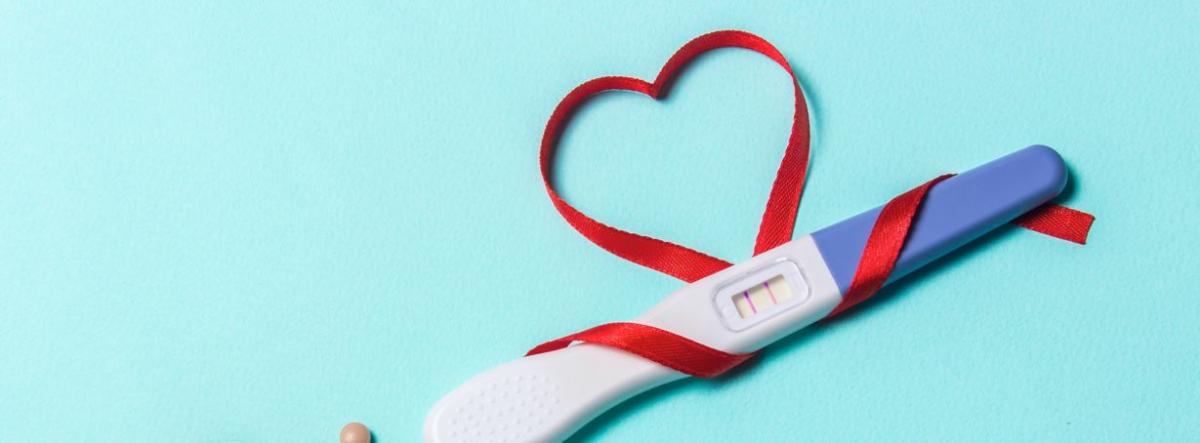 Positive pregnancy test stick with red ribbon making a heart