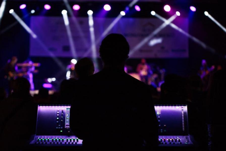 Silhouette of a man in front of a sound board with a concert going on in the background. 