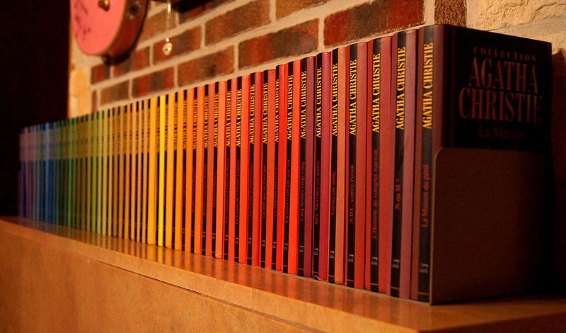 A row of Agatha Christie novels on a mantel piece making muted rainbow effect. 