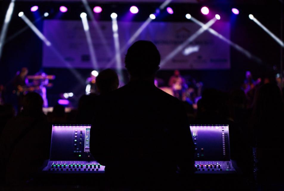 Silhouette of a man in front of a sound board with a concert going on in the background. 