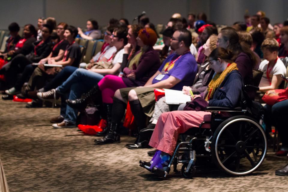 Image of crowd at a panel in colorful clothes and costumes, with a woman in a wheelchair at the end. 