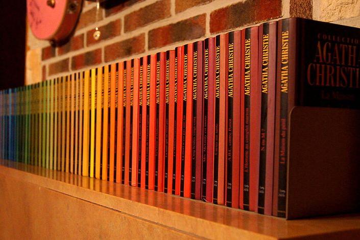 A row of Agatha Christie novels on a mantel piece making muted rainbow effect. 