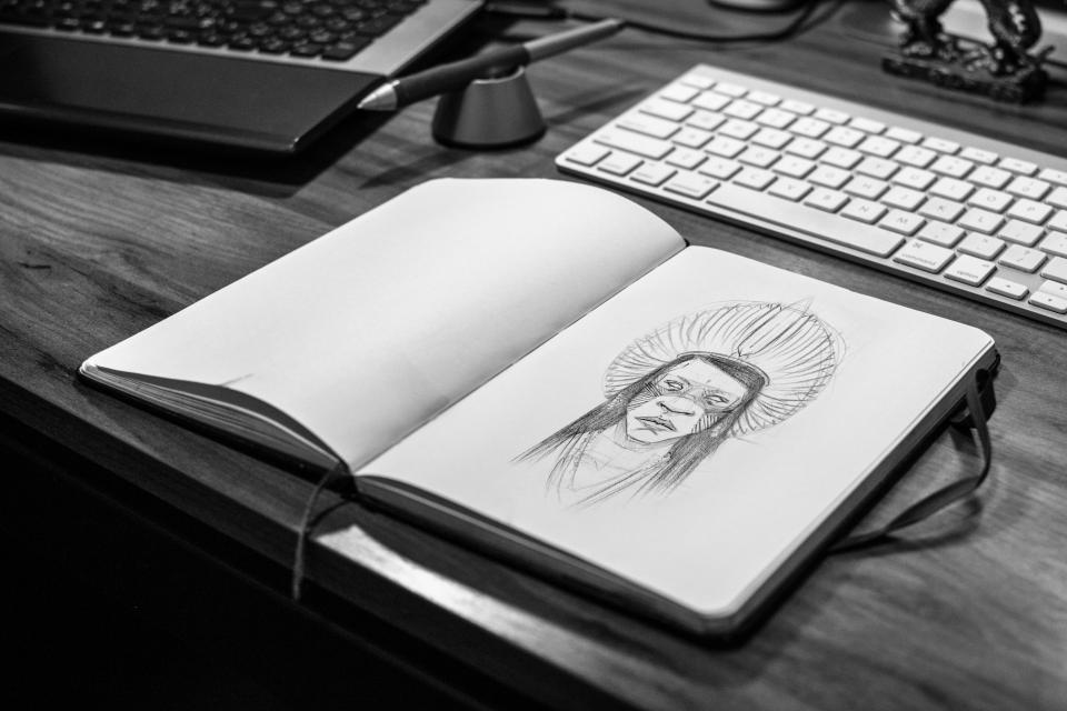 black and white photograph of a sketchbook with an illustration of an indigenous character on a desk
