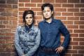 Cameron Esposito and River Butcher stand in front of a brick wall 
